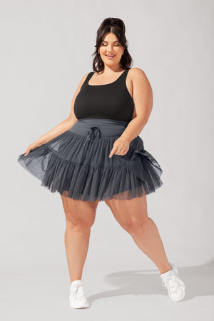 Woman wearing a black tank top and gray tutu skirt on a plain background