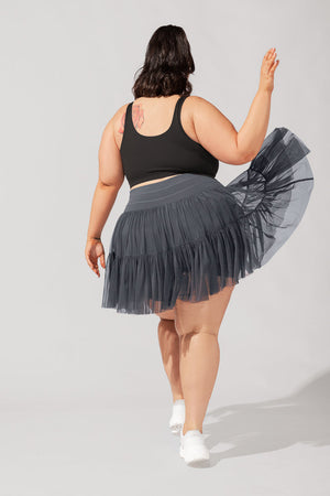Person wearing a black tank top and gray tulle skirt on a plain background