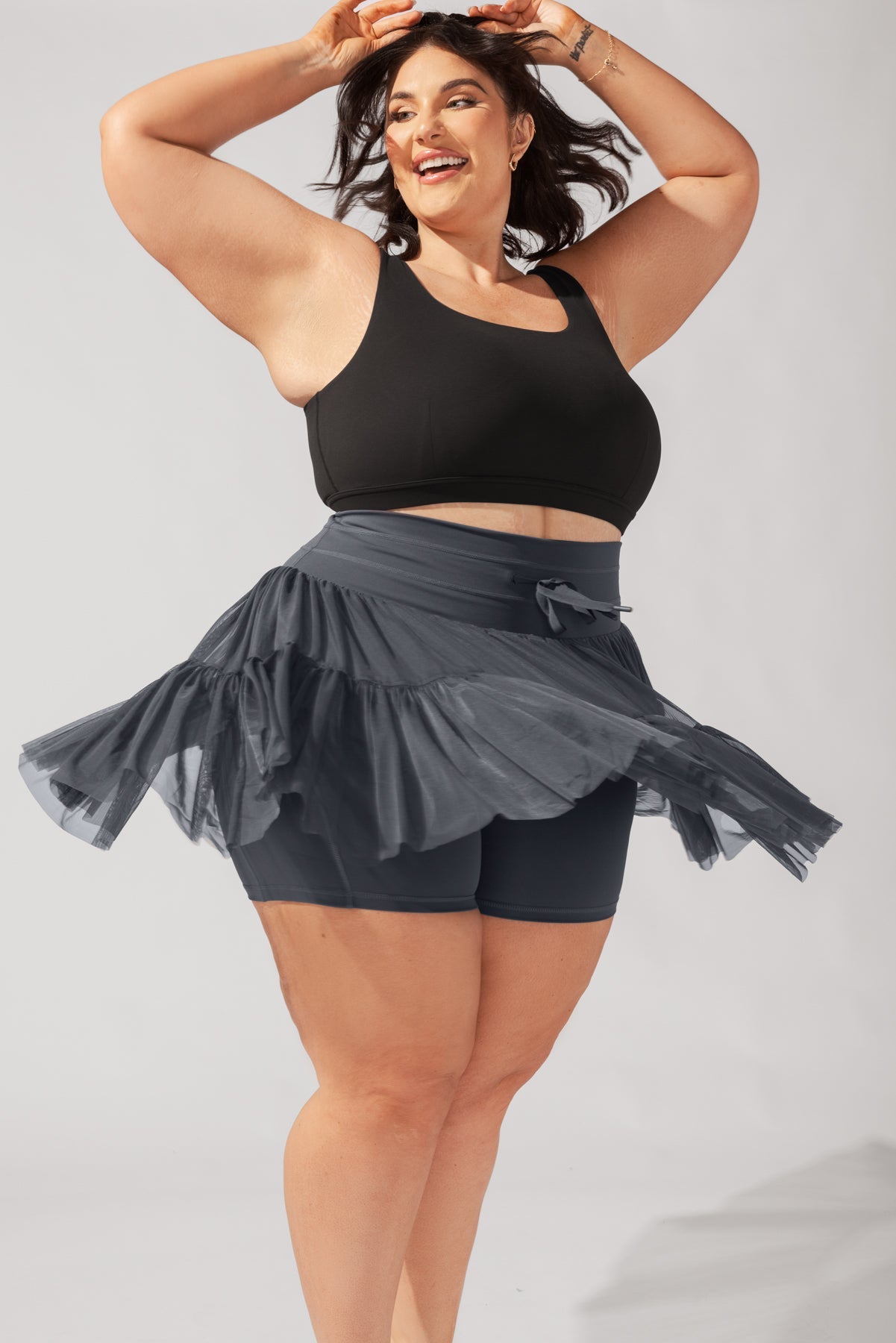 Woman wearing a black sports bra and gray skirt on a light gray background