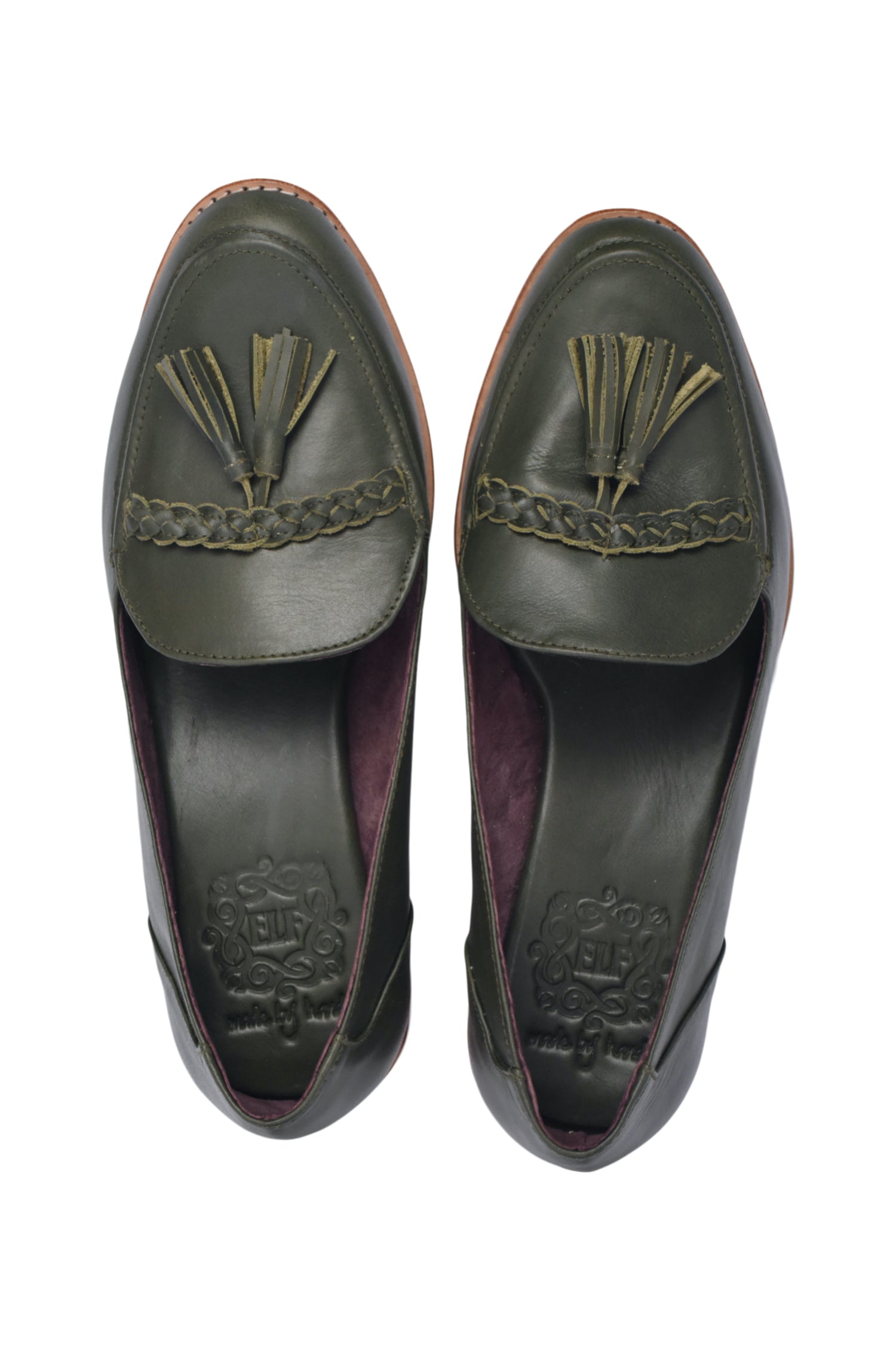 A pair of black leather loafers with tassels on the upper part, placed on a wicker surface. A person is in the process of fastening the shoes.
