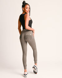 Woman wearing gray jogger pants and a black top on a white background