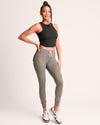 Woman wearing a black crop top and gray sweatpants on a plain background