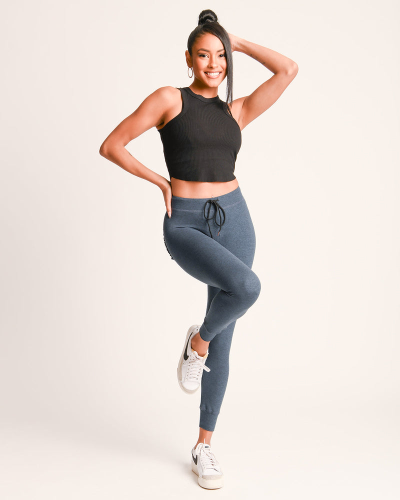 Woman wearing a black crop top and blue leggings on a light gray background