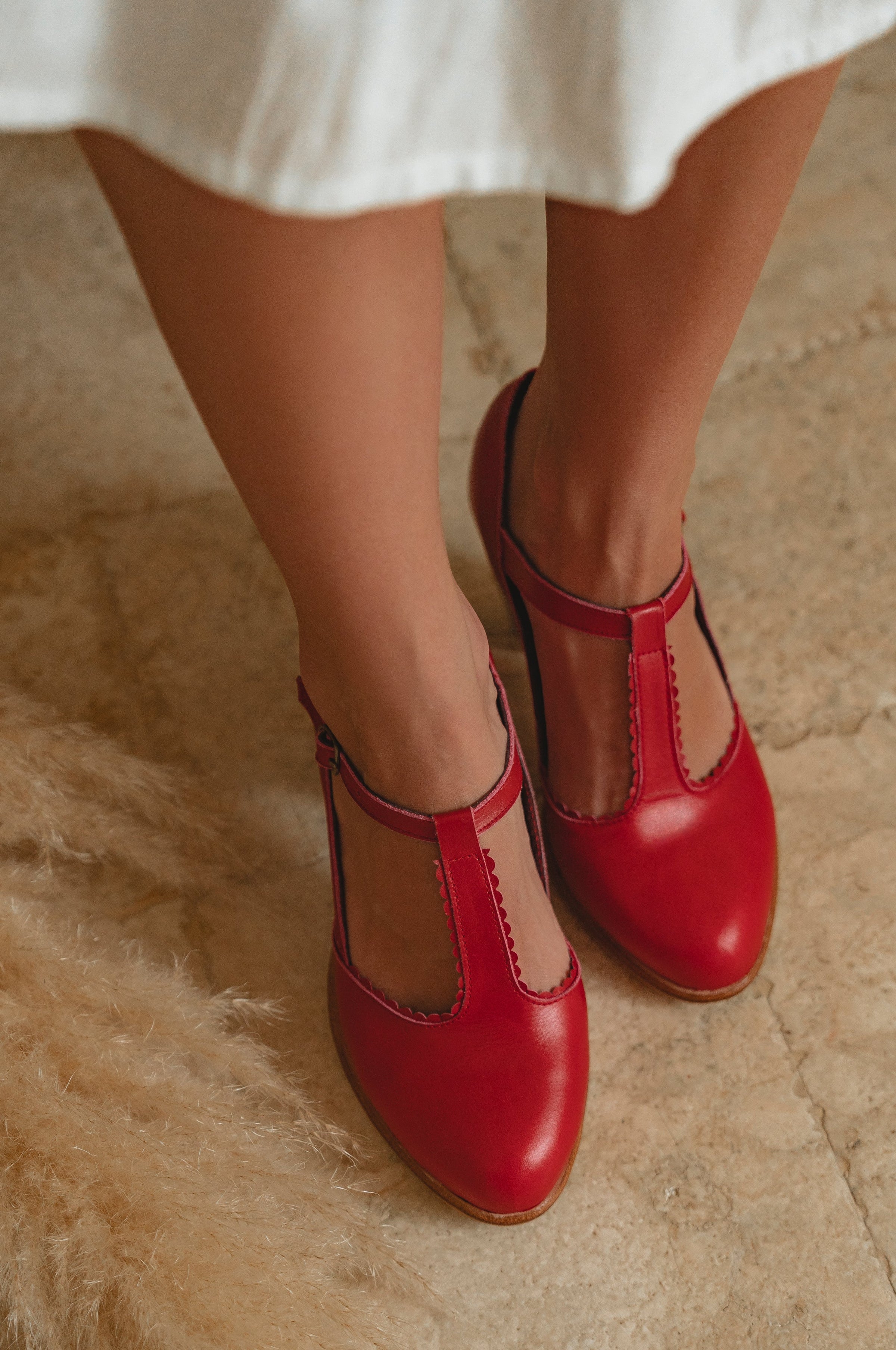 Red shoes worn with a white dress on a textured floor.