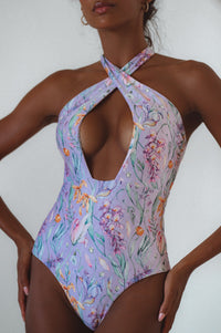 A woman wearing a black one-piece swimsuit with a halter neck and cross-over design at the front.