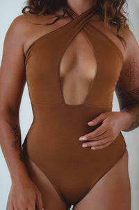 A model wearing a halter-neck, cross-over one-piece swimsuit with a plunging neckline and a high cut leg detail. The swimsuit has a multicolor floral print.