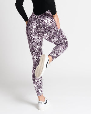 A pair of Dream Light Leggings with a snake print pattern, primarily in black with hints of lavender, paired with white sneakers.