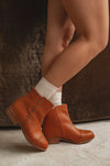 Brown leather ankle boots worn with white socks on a neutral background