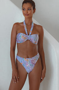 A high-waisted brown bikini bottom with a cheeky cut and a signature gold charm on the front.