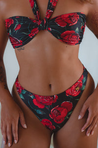 A high-waisted brown bikini bottom with a cheeky cut and a signature gold charm on the front.