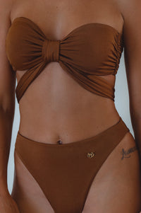 A bandeau bikini top in brown color, with a bow detail at the front, made from double-lined fabric, with a buckle back closure.