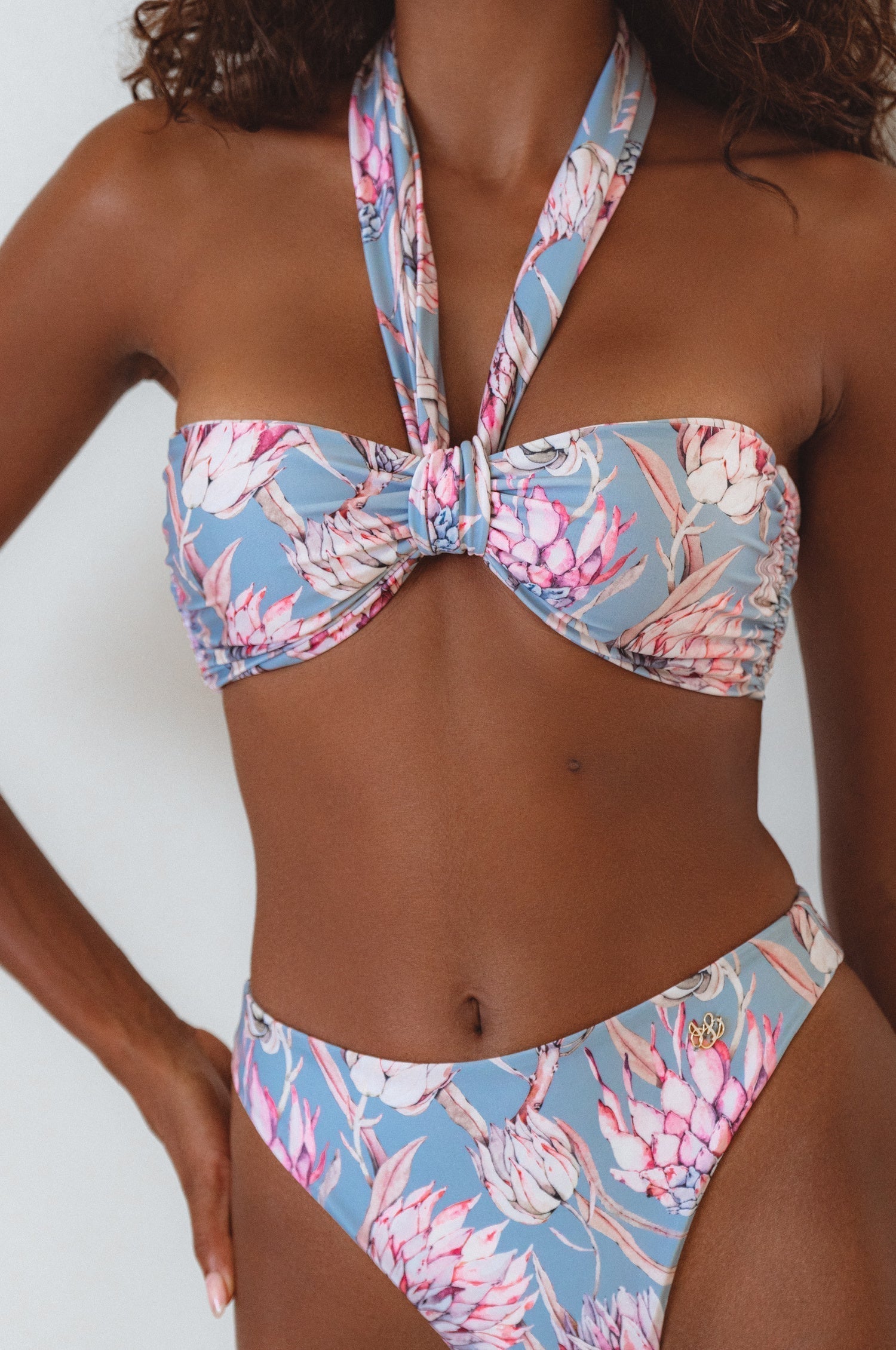 A bandeau bikini top with a floral print, featuring a wide tie strap that can be worn multiple ways, shown with the matching bikini bottom.