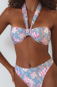 A bandeau bikini top with a floral print, featuring a wide tie strap that can be worn multiple ways, shown with the matching bikini bottom.