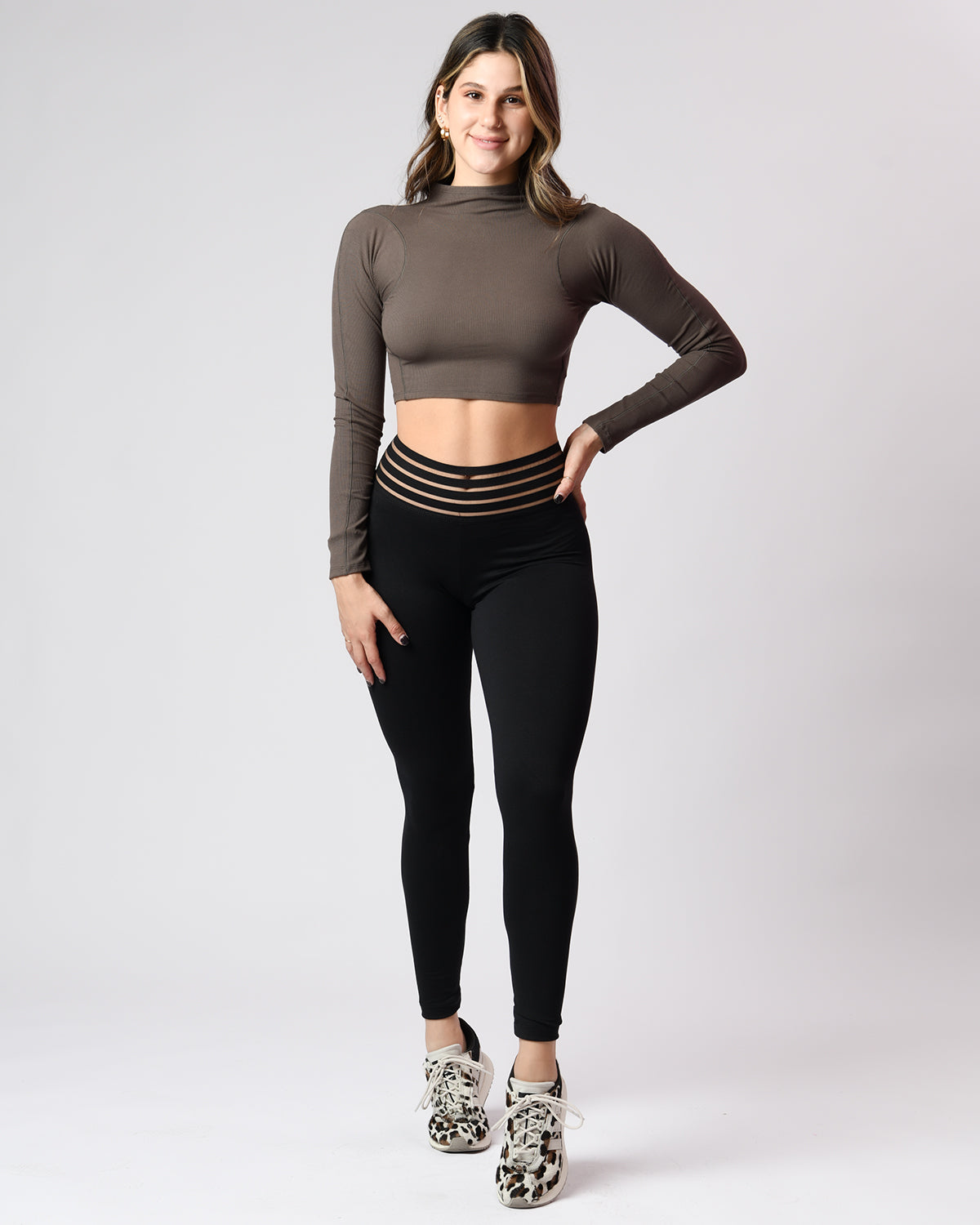 Woman wearing a brown long-sleeve crop top and black leggings on a white background