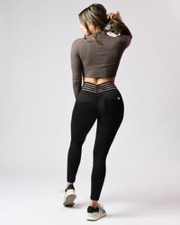 Person wearing a brown long-sleeve top and black leggings on a white background