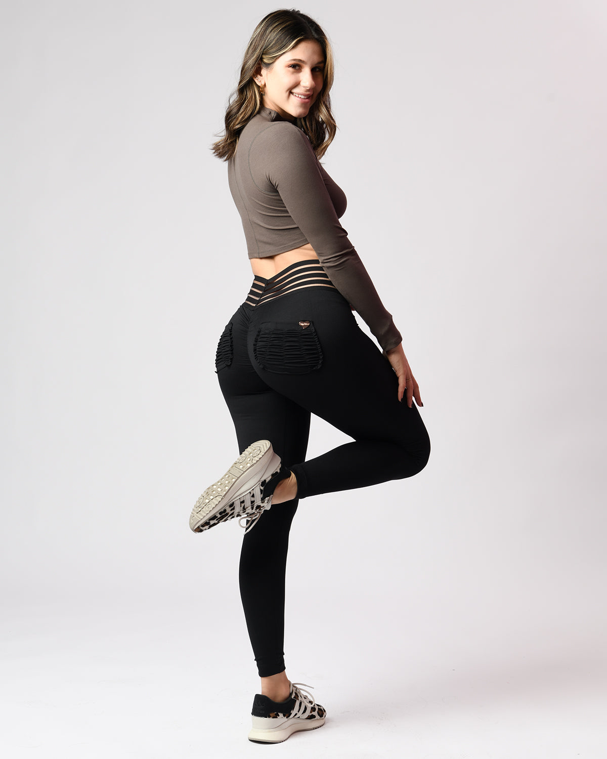 Woman wearing black leggings and a brown crop top on a white background
