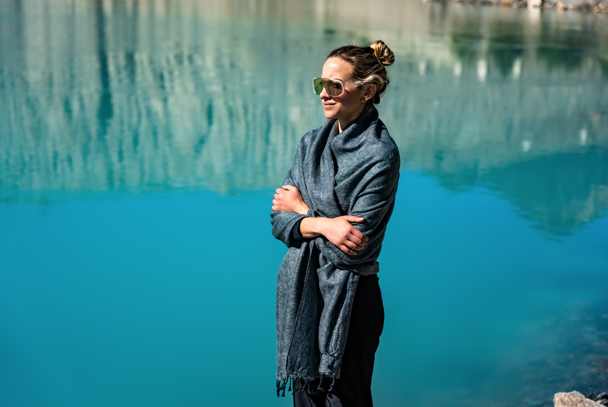 Woman standing by a lake wearing a gray coat and sunglasses.