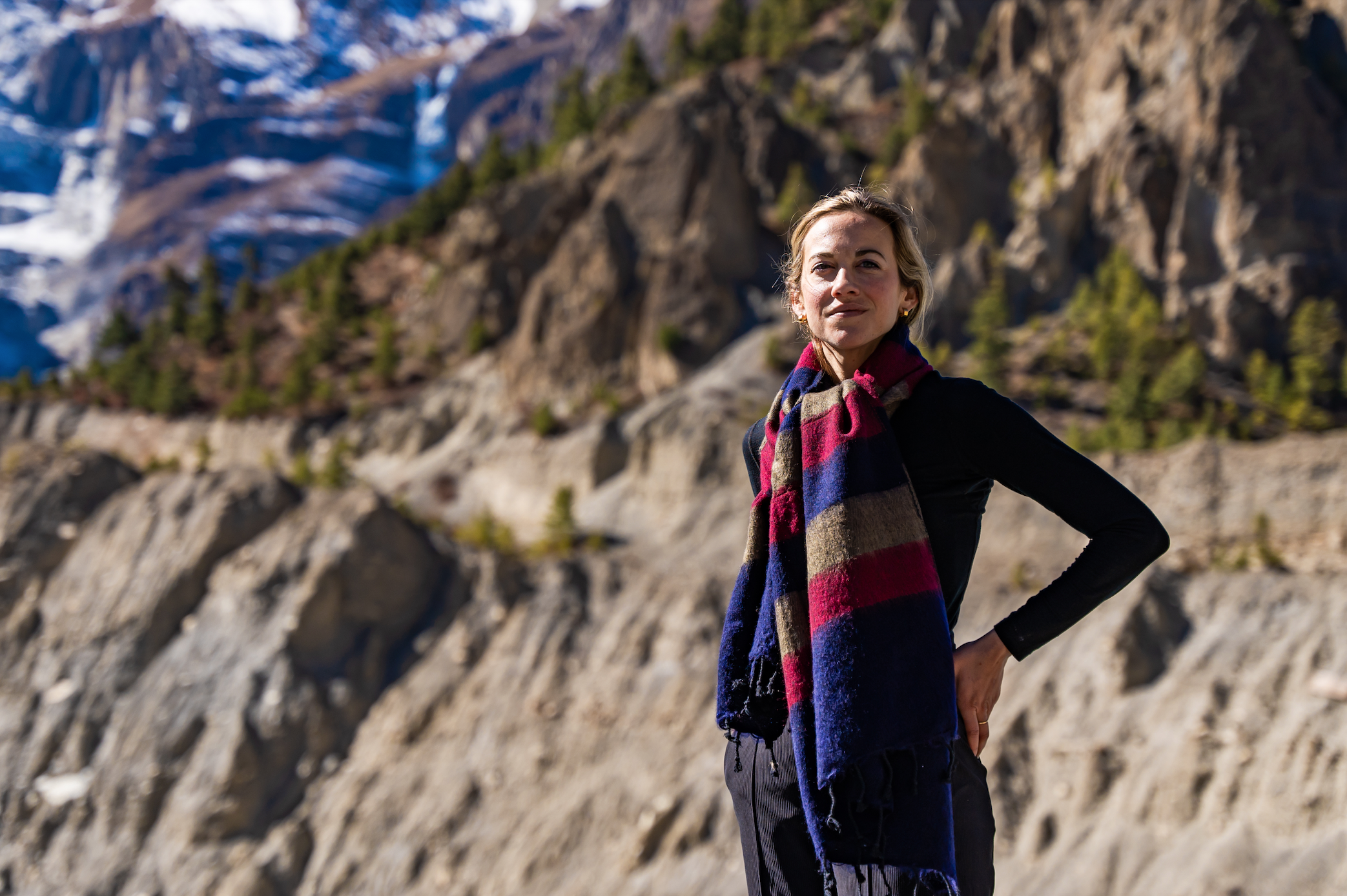 Person standing in a mountainous landscape wearing a colorful scarf