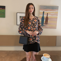 Woman in a floral blouse and black skirt standing in a room with paintings on the wall.