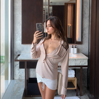 Woman taking a mirror selfie in a bathroom wearing a sheer top and white shorts.