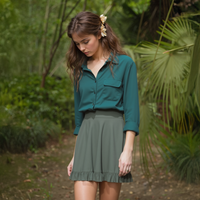 Woman in a green shirt and gray skirt standing in a forest setting