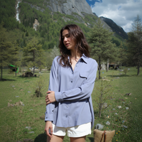 Woman in a blue shirt and white shorts standing in a grassy field with mountains in the background