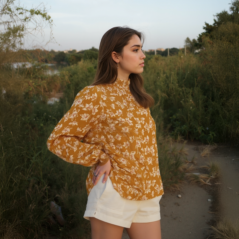 Woman in a yellow floral blouse and white shorts standing in a natural setting.