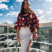 Woman in a floral kimono-style top and white skirt standing on a balcony with a cityscape background.