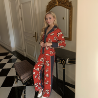 Woman in a red floral outfit standing in a room with a checkered floor and ornate mirror.