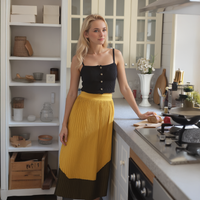 Woman standing in a kitchen wearing a black top and yellow skirt.