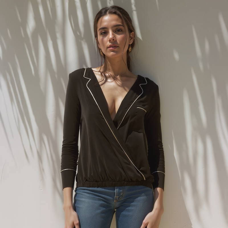 Woman wearing a black long-sleeve top with white piping and blue jeans against a light background