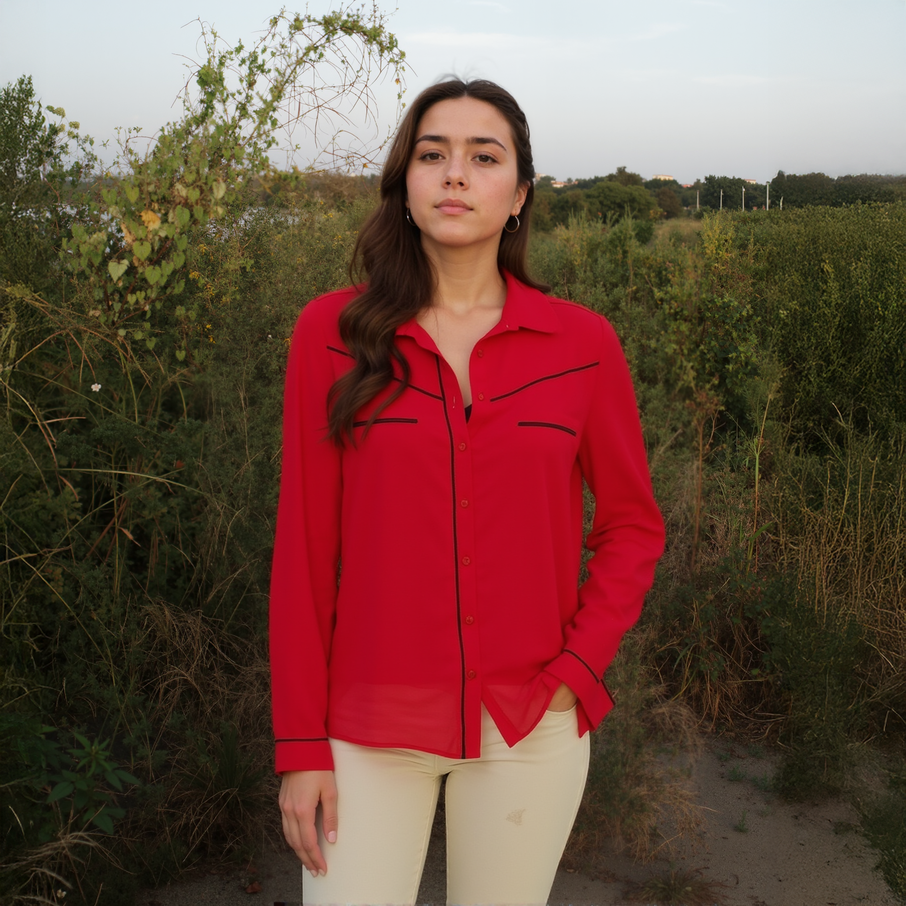 Woman wearing a red shirt with black trim standing in a natural setting.