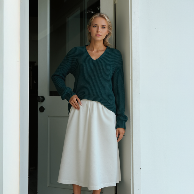 Woman wearing a teal sweater and white skirt standing in a doorway.
