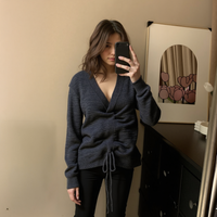 Woman taking a mirror selfie wearing a dark blue sweater in a room with a beige wall and a framed picture.