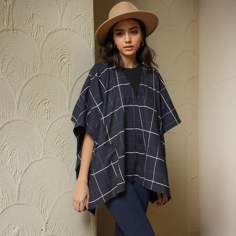 Woman wearing a navy checkered poncho and beige hat against a textured wall.