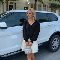 Woman in black top and white skirt standing next to a white car