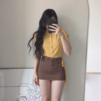 Person wearing a yellow shirt and brown skirt taking a mirror selfie.