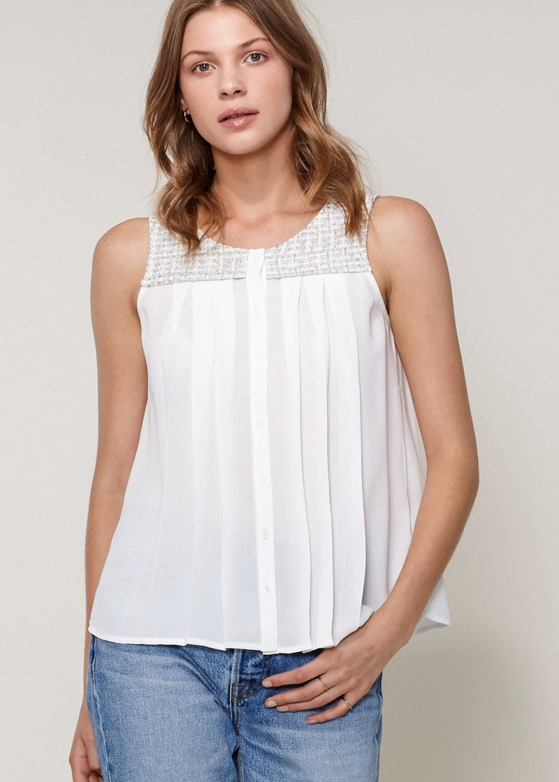 A woman wearing an ivory sleeveless tweed blouse with a pleated front and back, and a button fly closure.