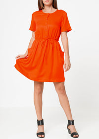 A woman modeling a short sleeve orange utility dress with side pockets and an elastic waistband.