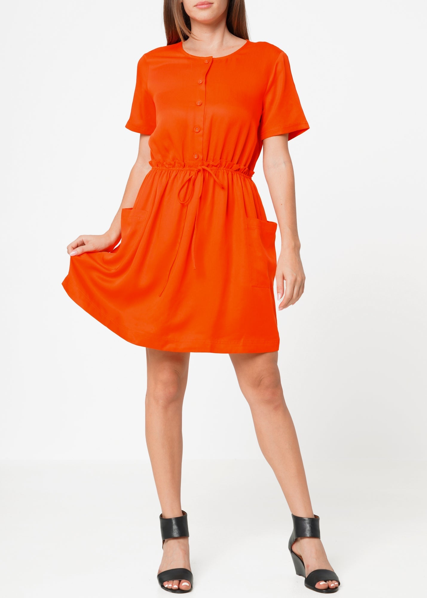 A woman modeling a short sleeve orange utility dress with side pockets and an elastic waistband.