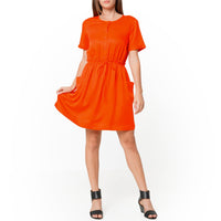 A woman modeling a short sleeve orange utility dress with side pockets and an elastic waistband.