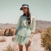 Woman in a light green dress and cap standing in a desert landscape