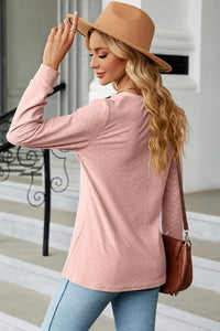 Woman wearing a pink sweater and tan hat, holding a brown handbag.