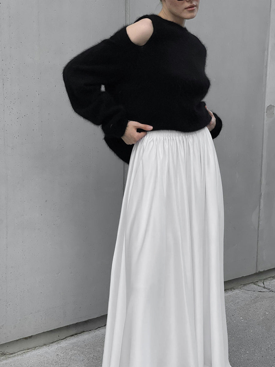 Person wearing a black sweater and white skirt against a gray wall.