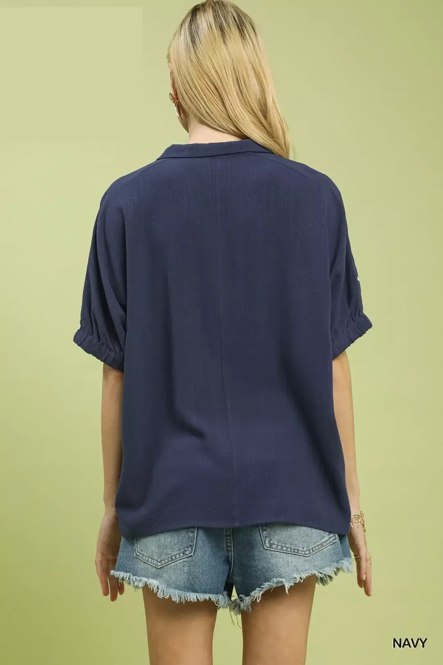 Person wearing a navy blue shirt and denim shorts on a light green background