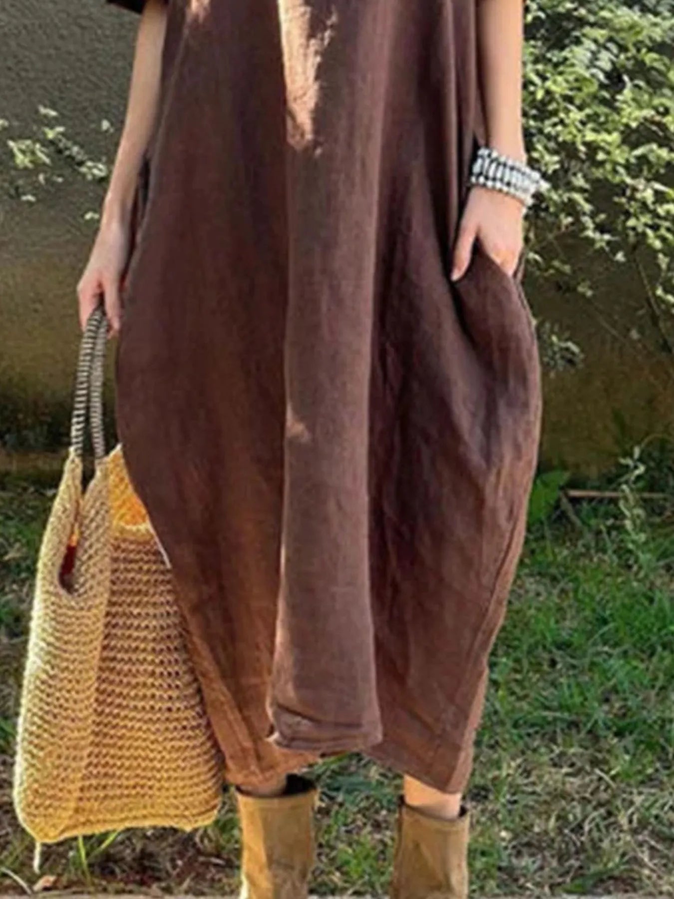 Person wearing a brown dress holding a yellow woven bag outdoors.