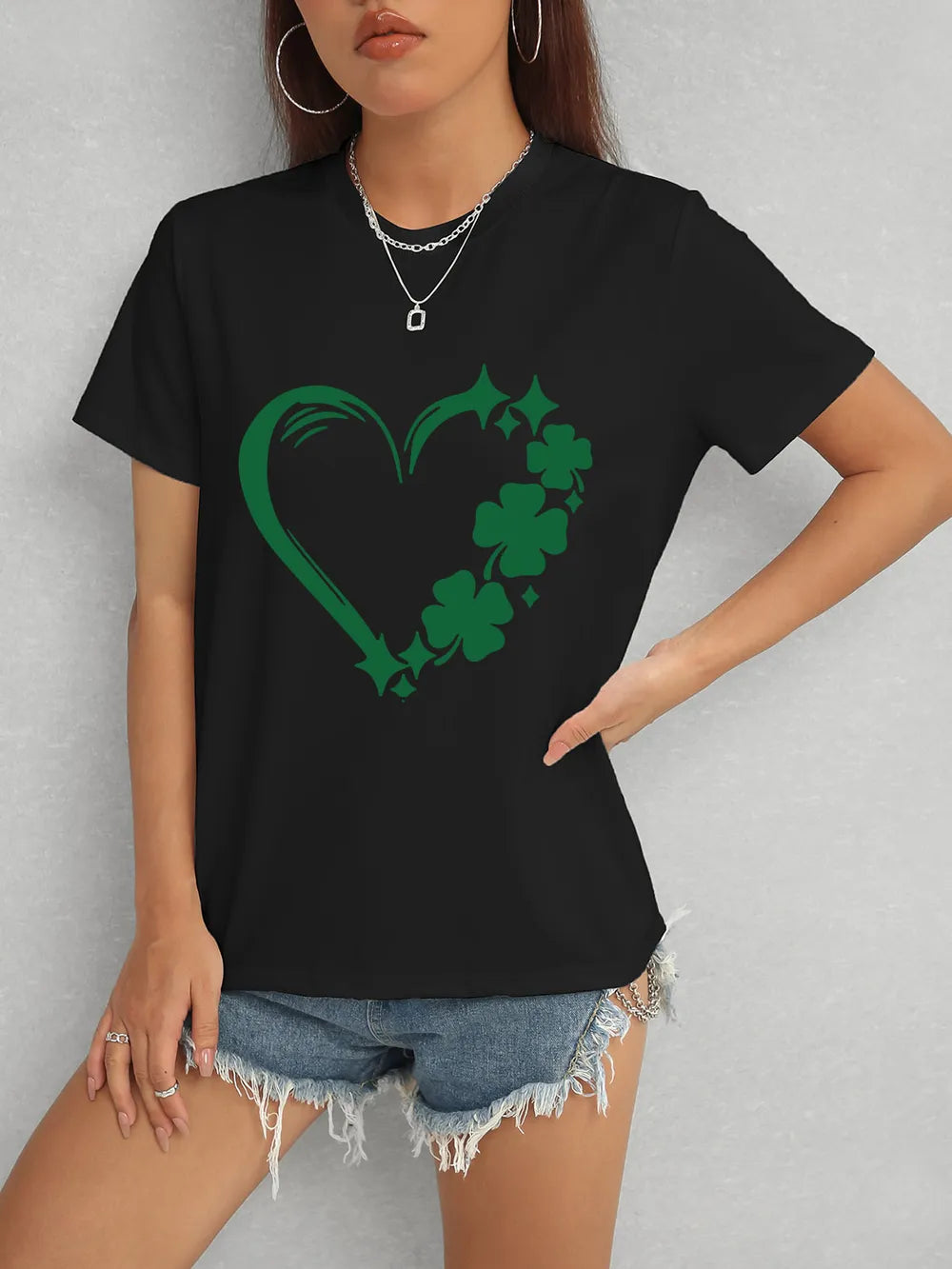 Person wearing a black t-shirt with a green shamrock heart design on a gray background