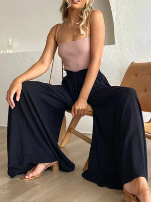 Woman sitting on a chair wearing a pink top and black wide-leg pants.