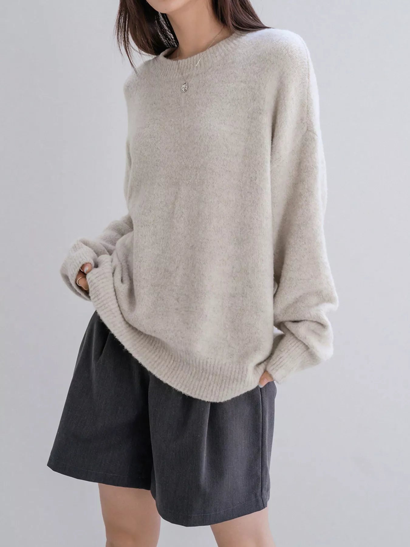 Person wearing a beige sweater and dark shorts on a plain background