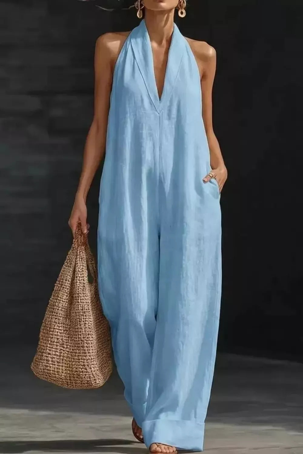 Woman wearing a light blue jumpsuit holding a woven bag against a dark background